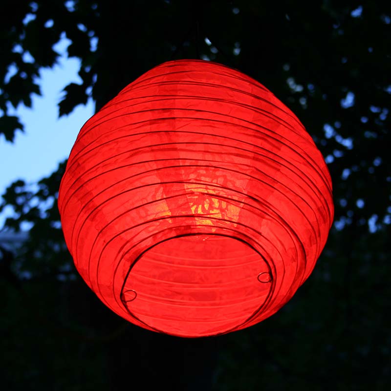 A red paper Chinese lantern hanging in a park.