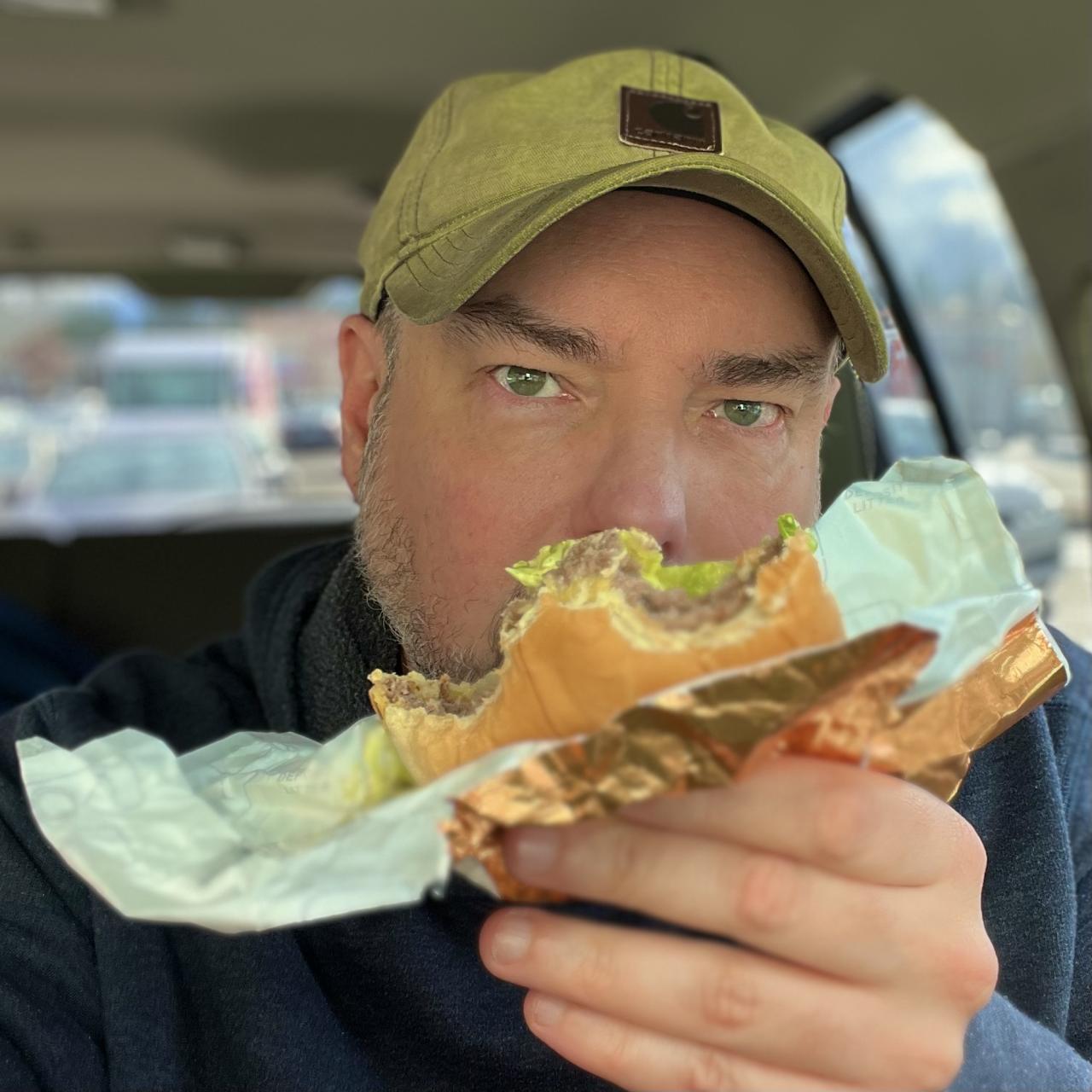 Matt Calkins holding a half-eaten Dick's Deluxe burger from Dick's Drive-In at Crossroads Mall in Bellevue Washington.