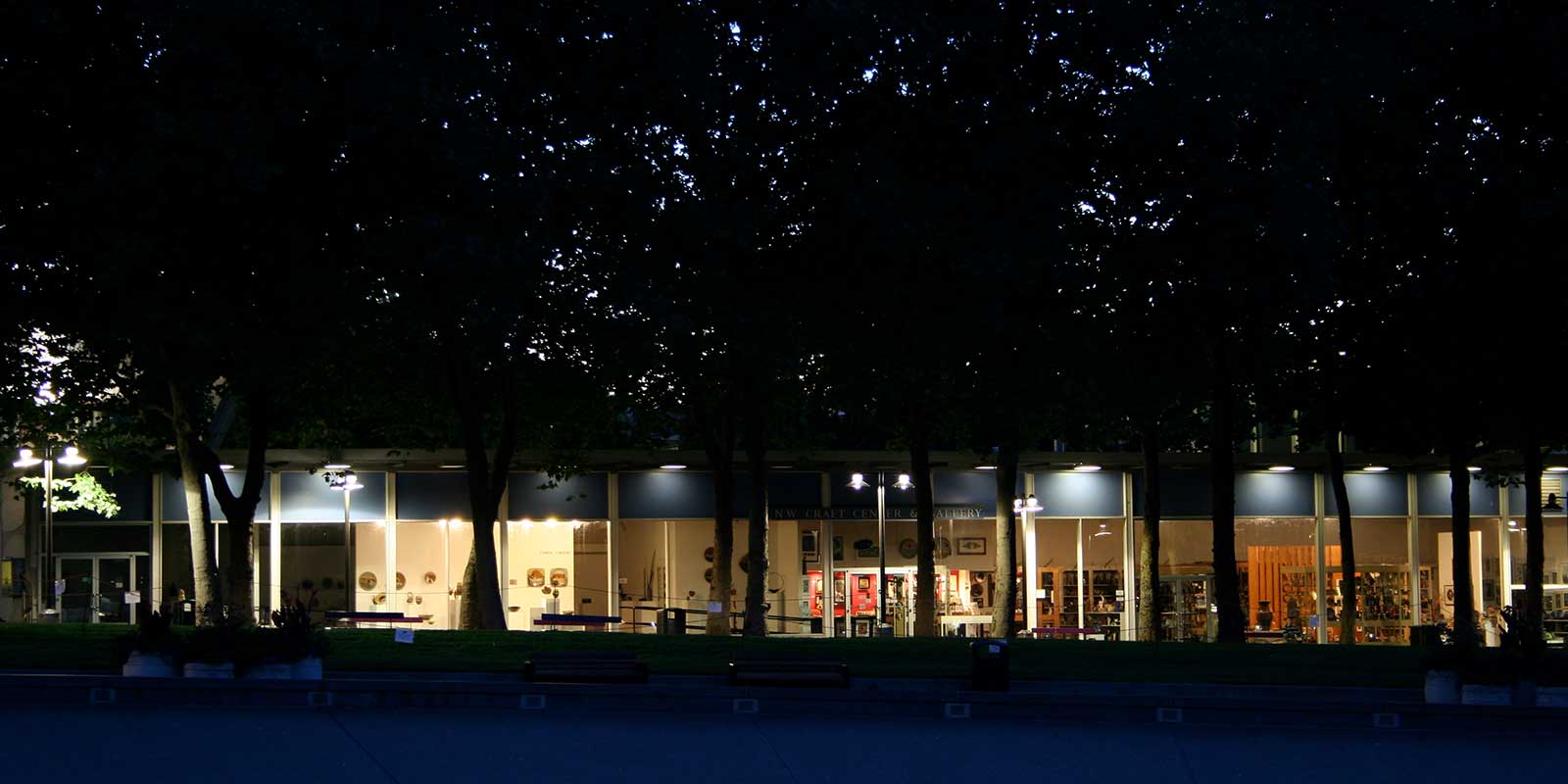 A dimly lit row of windows under trees showing artwork at Seattle Center.